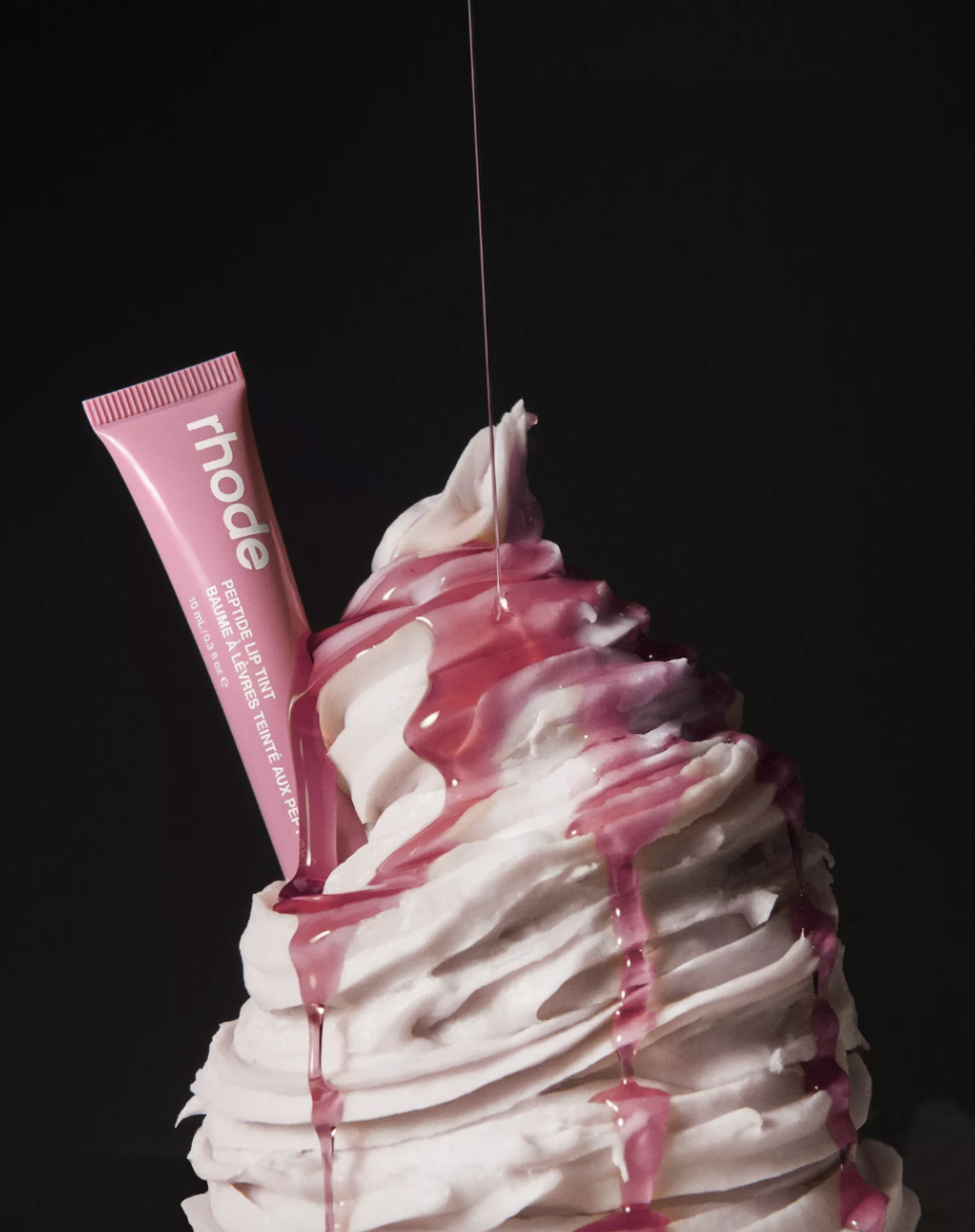 rhode lipgloss placed inside ice cream with a syrup being drizzled over it.